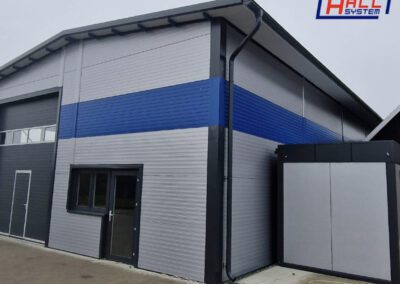 Priemyselná hala so sivým a modrým opláštením zo stenových sendvičových panelov s logom Hall System.
