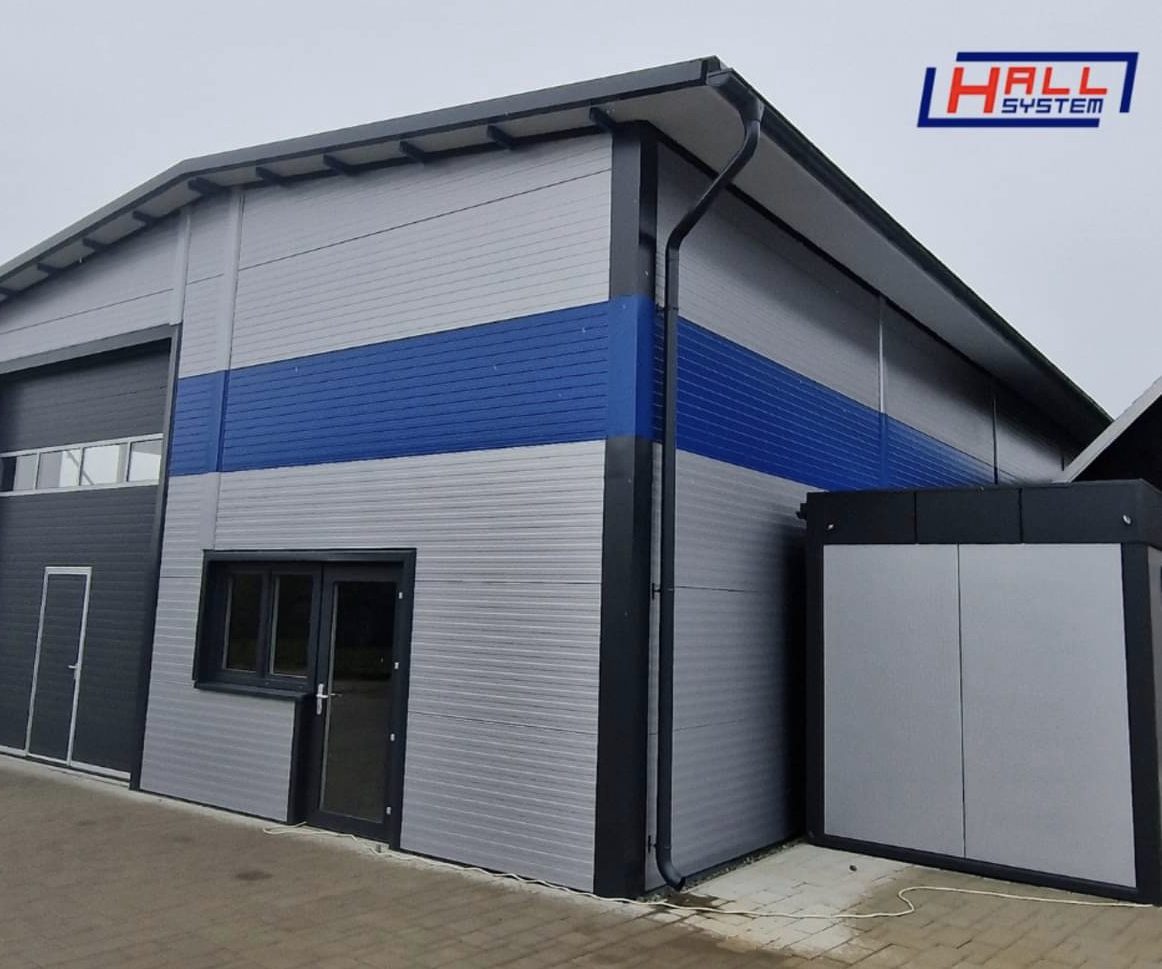 Moderná sendvičová hala s farebným prvkom Priemyselná hala so sivým a modrým opláštením zo stenových sendvičových panelov s logom Hall System.